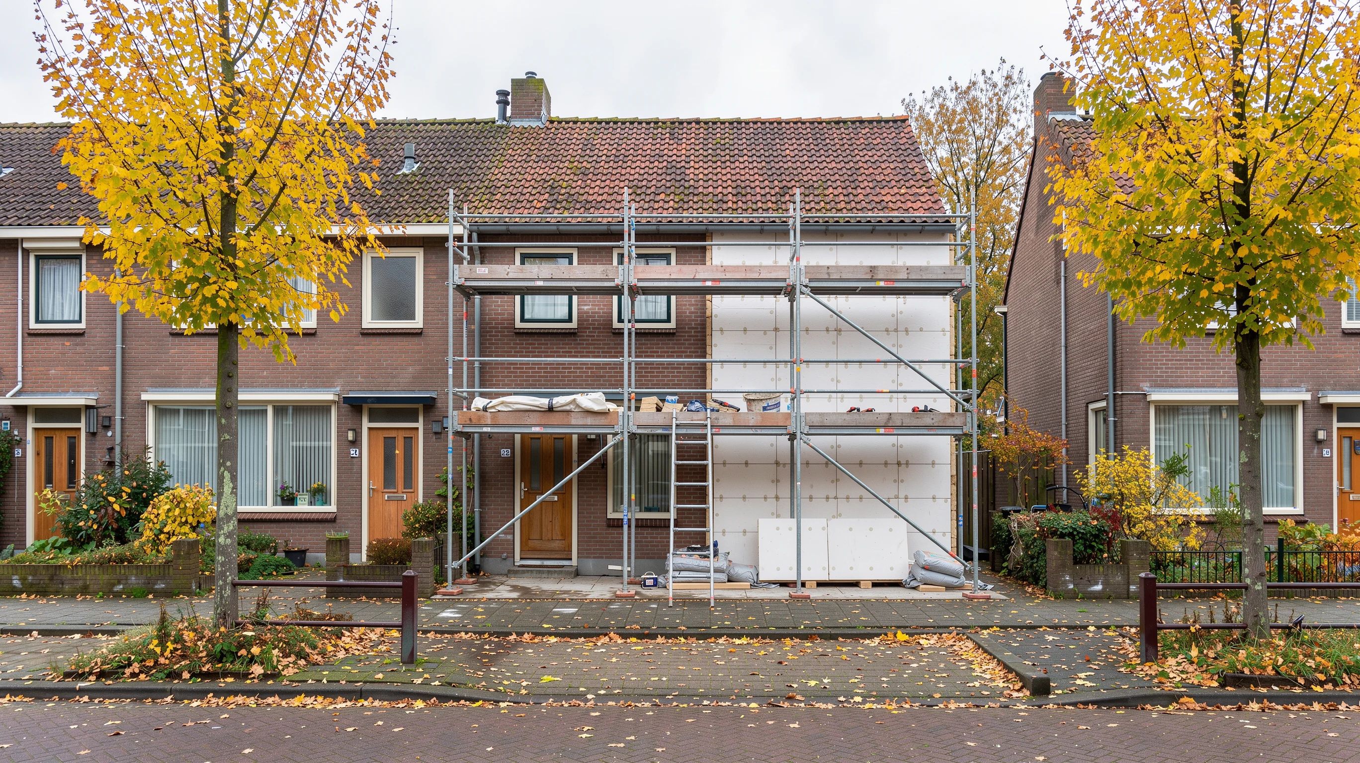 Rij rijtjeshuizen waarvan één huis in de steigers staat, de gevel half bekleed met witte isolatieplaten