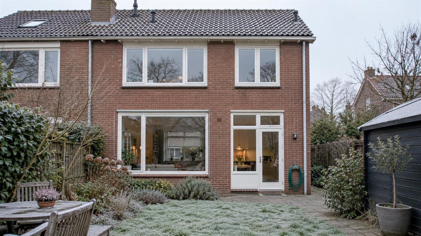 Achtergevel van een jarendertigwoning met ramen van isolatieglas in witte houten kozijnen, met rijp op het gras