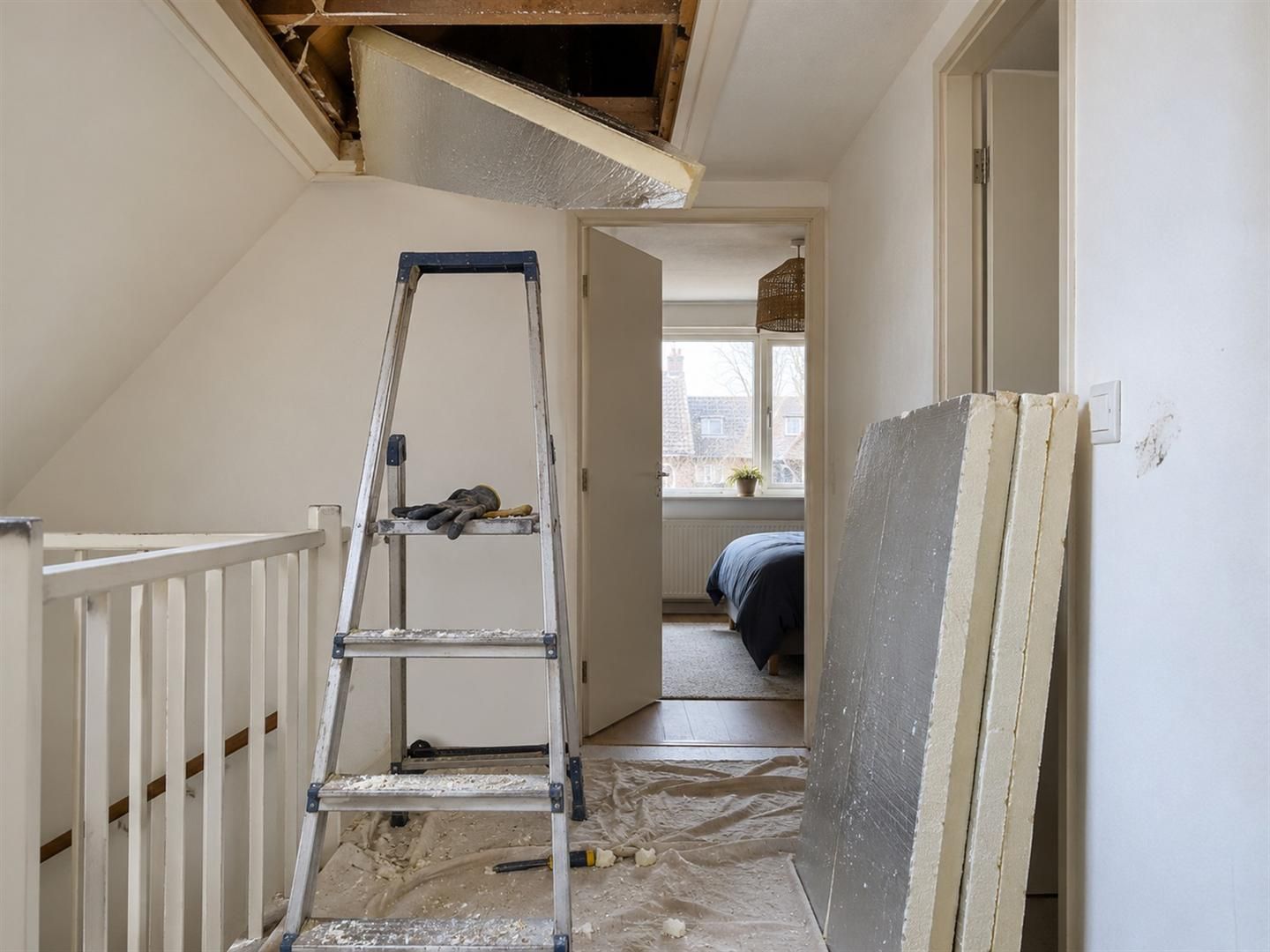 Trapje onder een open zolderluik, een PIR-plaat half door de opening en een stapel platen op de overloop