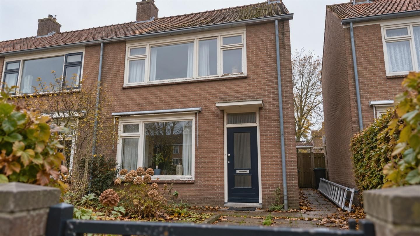 Jarenvijftig rijtjeshuis vanuit de voortuin, met pannendak, oude houten kozijnen en herfstblad op het pad